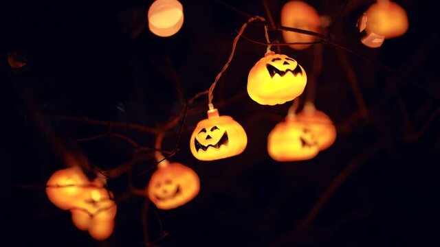 Halloween pumpkin garland on a tree. A glowing pumpkin on a dark background.