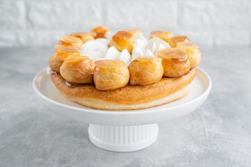 Saint Honore cake with profitrols, caramel, custard and whipped cream on a white plate on a gray concrete background. Traditional French dessert. Copy space.