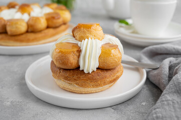 Saint Honore cake with profitrols, caramel, custard and whipped cream on a white plate on a gray concrete background. Traditional French dessert. Copy space.