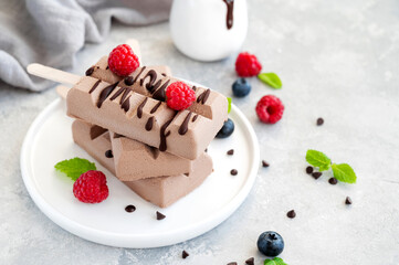 Homemade chocolate ice cream (popsicles) with fresh raspberry and blueberry on a plate on a gray background. copy space.
