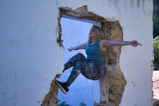 Young Blonde Woman In Sportswear, Doing Calisthenics Exercises In A Window Of A Dilapidated Building. Concept, Calisthenics, Fitness, Exercise, Curvy Girl.