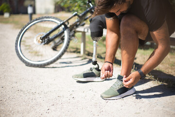 Close-up of person with disability tying laces. Man with mechanical leg getting ready for riding...