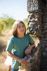 Dreamy boy near castle wall. Child in green t-shirt looking up, thinking. Childhood, nature, fantasy concept