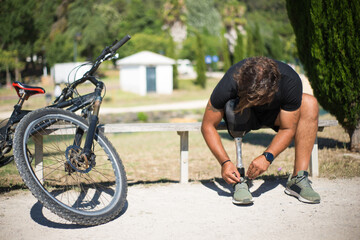 Curly person with disability tying laces. Man with mechanical leg getting ready for riding bicycle....