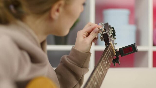 Close-up girl hands tuning guitar. Young woman checking pegs of acoustic guitar. Female guitarist tuning sound of musical instrument. Lady holding string instrument in hands.