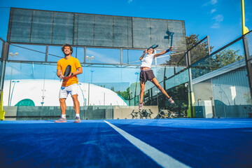 Mixed padel match in a blue grass padel court - Beautiful girl and handsome man playing padel...