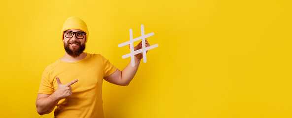 smiling bearded man pointing on hashtag over yellow background, panoramic layout