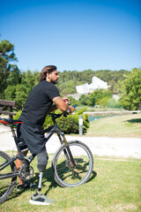 Side view of man with mechanical leg on bicycle. Thoughtful person with disability sitting on bicycle, phone in hands. Sport, disability concept