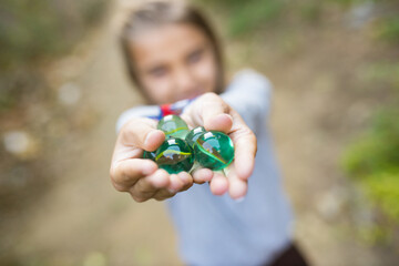 Close-up of marble balls in girls hands. Child in grey longsleeve showing green marbles at camera....
