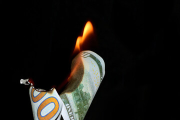 A hundred dollar bill in American US currency is on fire on a black background