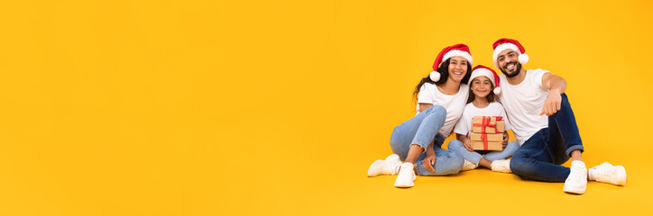 Fototapeta premium Arabic Family Posing Holding Xmas Gifts Wearing Santa Hats, Studio