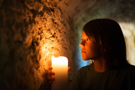 Courageous little boy exploring old castle. Dark haired boy holding candle in dark tunnel. Childhood, nature, fantasy concept