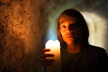 Bold little boy exploring old castle. Dark haired boy holding candle in dark tunnel, looking at...