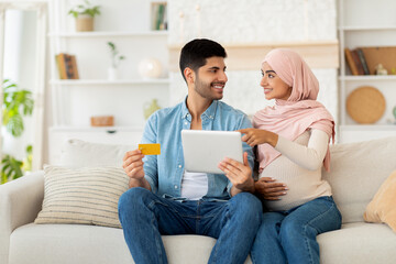 Pregnancy and online shopping concept. Muslim pregnant spouses using digital tablet and credit card purchasing goods