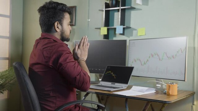 Worried trader praying god to make profit or stock market to go up infront of charts on computer screen - Concept of risk in crypto trading and investing on equity shares