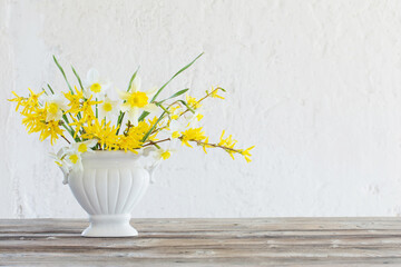 white and yellow spring flowers in vase on background old white wall