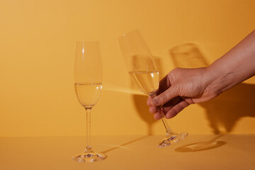 Two glasses of champagne with a toast gesture with yellow background and reflected shadows