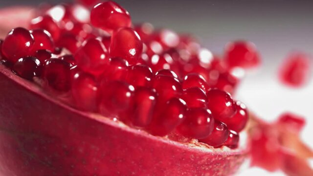 Pomegranate Grains rolls down on surface of broken pomegranate in slow motion