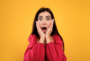 Unbelievable. Shocked armenian lady with open mouth and hands on cheeks posing over yellow...