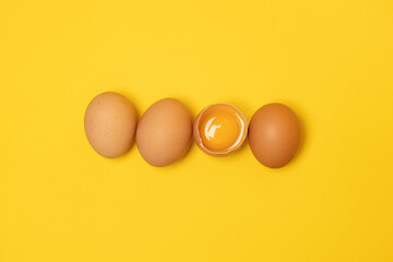 Brown chicken eggs and one broken egg with yolk on yellow background. Minimal summer background.