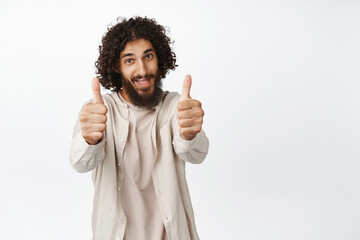 Handsome middle eastern man look proud, showing thumbs up in approval, like and agree, praise smth...