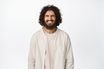 Image of sad and gloomy middle eastern guy feeling pain, crying and clenching teeth, standing distressed against white background