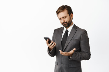 Image of displeased businessman looking at mobile phone app screen and grimacing slightly disappointed, checking applications stats, white background