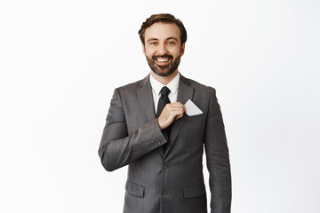 Handsome bearded corporate man put credit card in suit pocket, smiling pleased, concept of money and investments, white background
