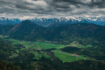 Snow covered Bavarian Alps with dramatic dark clouds, green forest at valley of Jachenau near Lake Walchensee, Bavaria.
