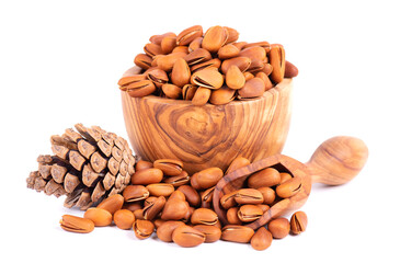 Pine nuts in olive bowl, isolated on white background. Pine cones and heap of roasted pine nuts in shells.