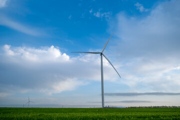 Wind power plant on agricultural field against the background of blue sky with clouds.