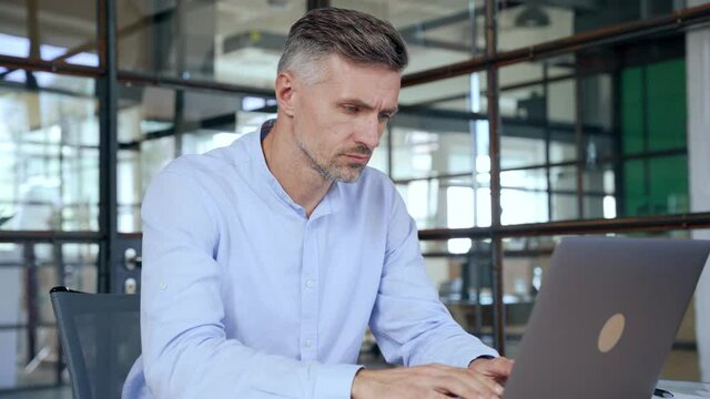 Focused busy mature business man lawyer ceo trader using computer, typing, working in modern office room doing online data market analysis, thinking planning tech strategy looking at laptop.