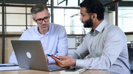 Two diverse business men analysts partners talking, working together, discussing data management using laptop computer. Indian manager consulting client with online technology at office meeting.
