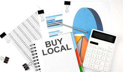 Text BUY LOCAL on a notebook on the diagram and charts with calculator and pen