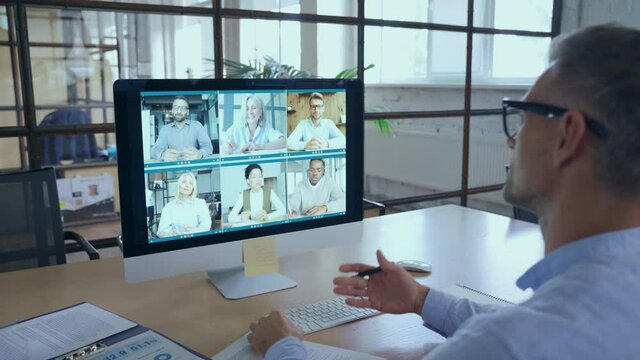 Business man talking with diverse team people having digital group video call global conference working leading online virtual meeting training on pc computer. Over shoulder videocall screen view