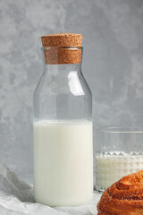 Food photo composition. Fresh white bread bun with sugar on a gray background. Nearby is a glass of milk.