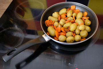 Pommes de terre et carottes cuisinées dans une poêle sur une table de cuisson