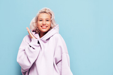 Young beautiful smiling female in trendy summer hoodie. Sexy carefree woman posing near blue wall...