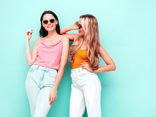 Portrait of two young beautiful smiling brunette hipster female in trendy summer clothes. Sexy carefree women posing near blue wall. Positive models having fun. Cheerful and happy