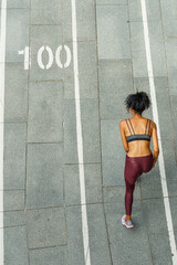 Strong woman in stylish tracksuit runs along stadium track view from above. Development and achievement concept