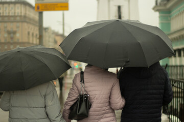 Family with black umbrellas. People rain. Parents with their daughter walk around the city.