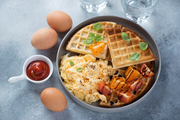 Plate of waffles served with scrambled eggs and cherry tomatoes, elevated view on a light-blue stone background