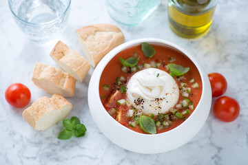 Gazpacho made of red tomatoes and served with burrata cheese, studio shot on a light-grey marble background, elevated view