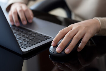 Closeup business person hand using wireless mouse and work with laptop computer at modern office desk.