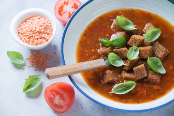 Plate of tomato and lentil soup topped with croutons and fresh green basil, selective focus, close-up