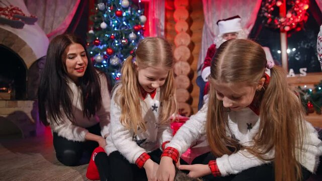 Little girls with a grey kitten at Christmas. Santa Claus brings a cat to children as a present for New Year. Happy kids with a little kitty in the decorated house at Christmas.