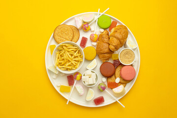 French croissant, candy on a stick, jelly candies, marshmallows, cookies and macarons on a yellow bright background. Unhealthy foods on colored background, top view.