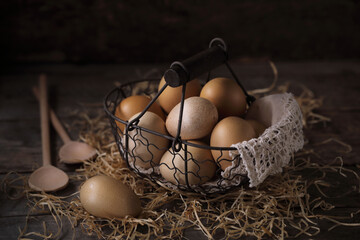 Still life with fresh chicken eggs in a wicker basket on a wooden table.