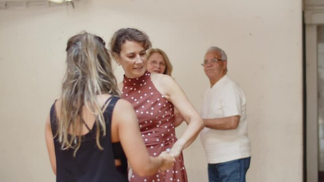 Slow motion of teacher dancing with woman attending class. Excited senior people in activewear rehearsing dance movements in pairs, having master class in ballroom. Hobby, fitness concept