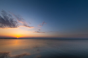 Beautiful, colorful sunset, sunrise over a wide river. Twilight rays and clouds reflected in the calm water. 